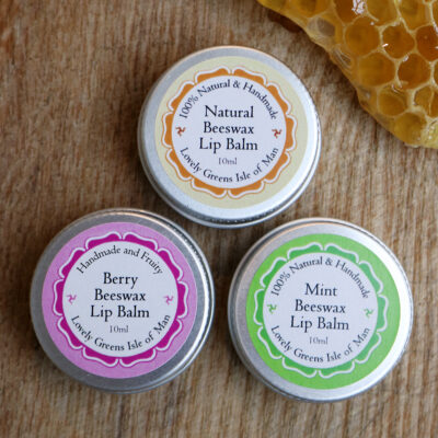 Three lip balms in small round steel pots with colorful labels.
