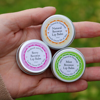 Three lip balms in small round steel pots with colorful labels.