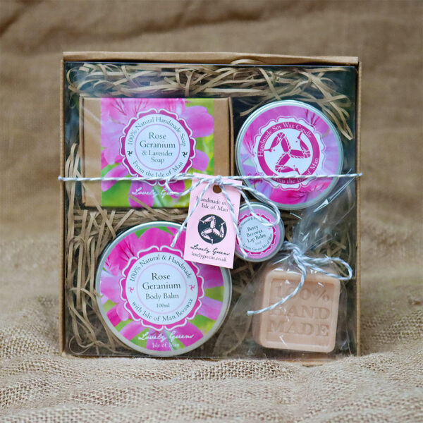 A collection of rose geranium scented products including a soap, candle, and body balm. Also included are a berry lip balm and additional pink soap. The entire collection has pink labels.